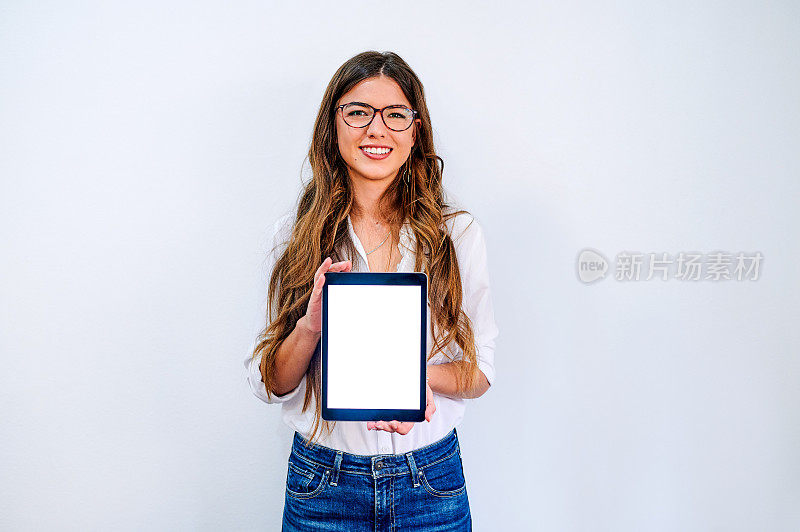 照片中，一位迷人的年轻女商人独自站在一堵白墙上，手里拿着一台数码平板电脑