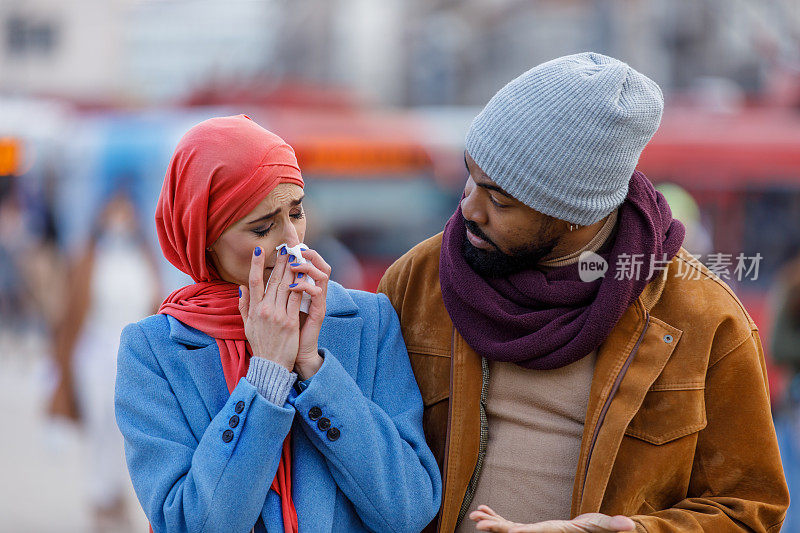 一位患季节性流感的妇女和她的丈夫在市区散步，并用纸巾咳嗽。