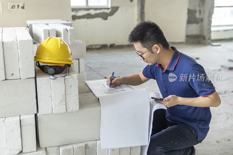 亚洲男性工程师，在装修工地处理建筑图纸和手机