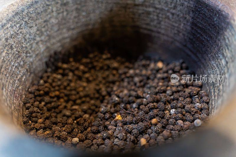 灰浆里的黑胡椒粒。研磨黑胡椒和黑胡椒颗粒为背景特写，质地，香料药用特性。食品与健康理念。