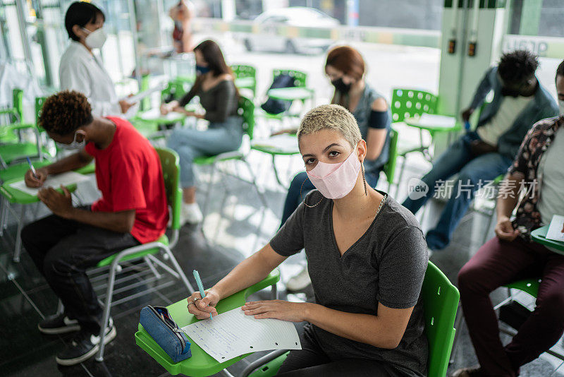 图为一名女学生戴着口罩在教室里考试