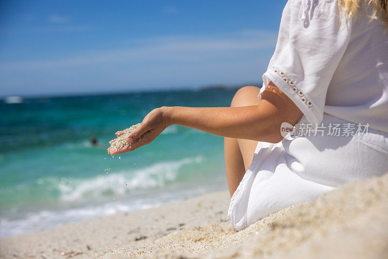 在意大利撒丁岛的海滩上，女人的手在玩沙。