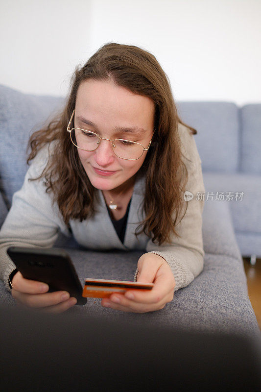 沙发上的女人用手机上网购物，检查信用卡号码