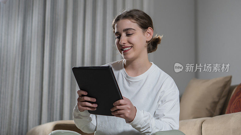 微笑的年轻女子看着她的平板电脑的肖像。和她视频聊天的女孩是快乐的。