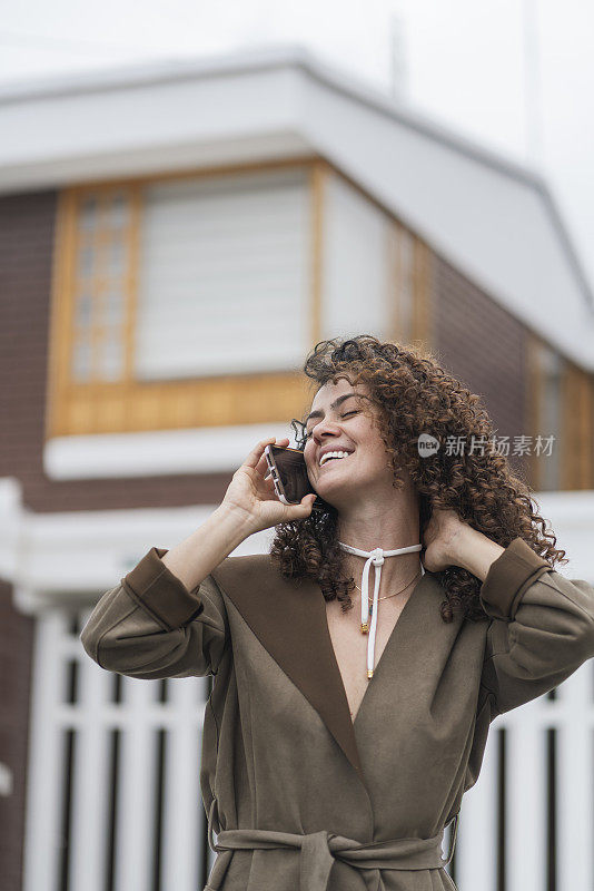 一头卷发的拉丁女子正在屋外用手机打电话