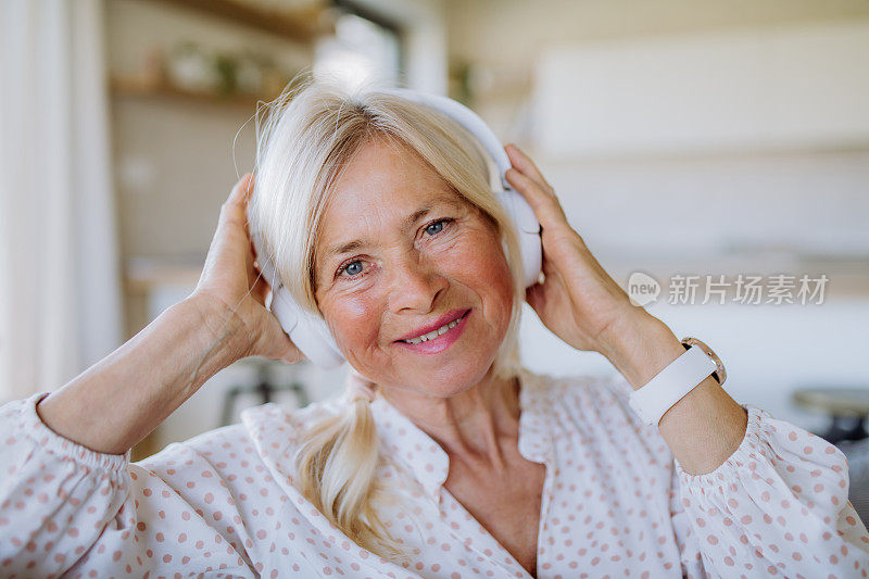 老妇人戴着耳机在家听着放松的音乐