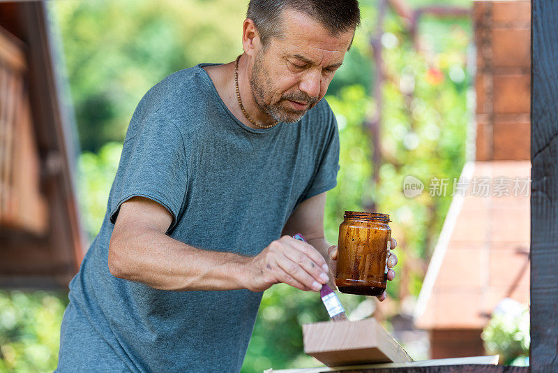 在阳光明媚的日子里，男人正在为家里的露台粉刷木板