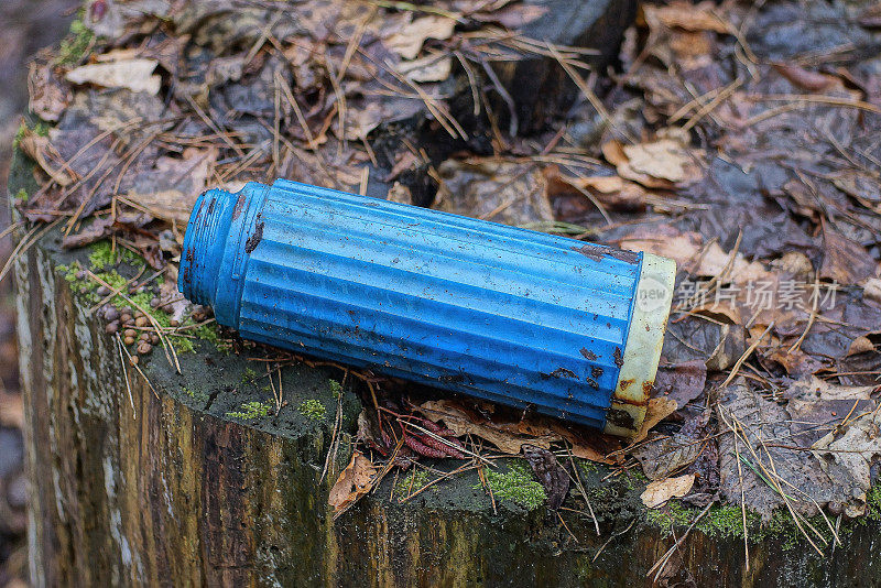 一只又旧又脏的蓝色塑料保温瓶躺在灰色的木桩上