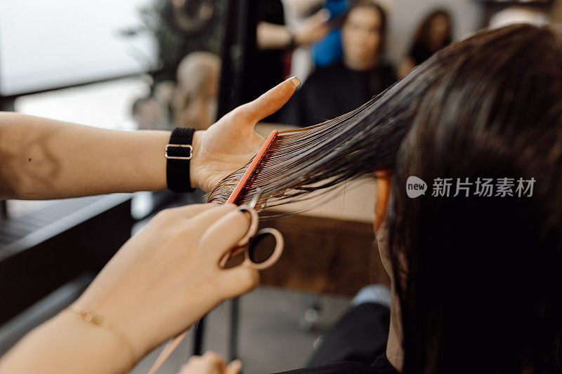 剪裁照片的女美容师做发型刷长湿头发与粉红色的梳子，在美容院拿着剪刀。