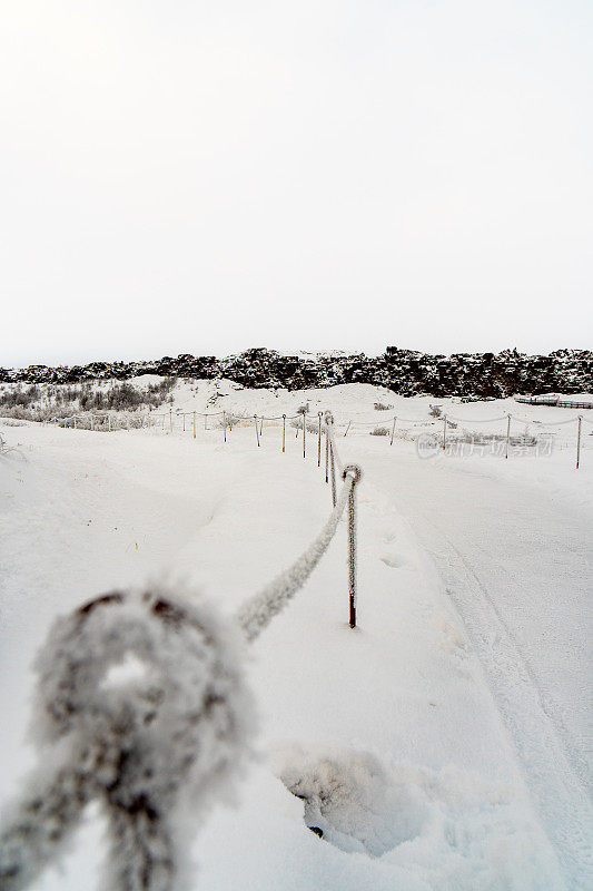Thingvellir国家公园的欧亚和美洲构造板块旁边，完全被冰雪覆盖的小路和铁栅栏，天空完全是白色的。