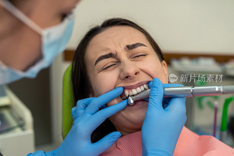在现代化的牙科诊所里，医生用牙钻给她的年轻女子治疗牙齿