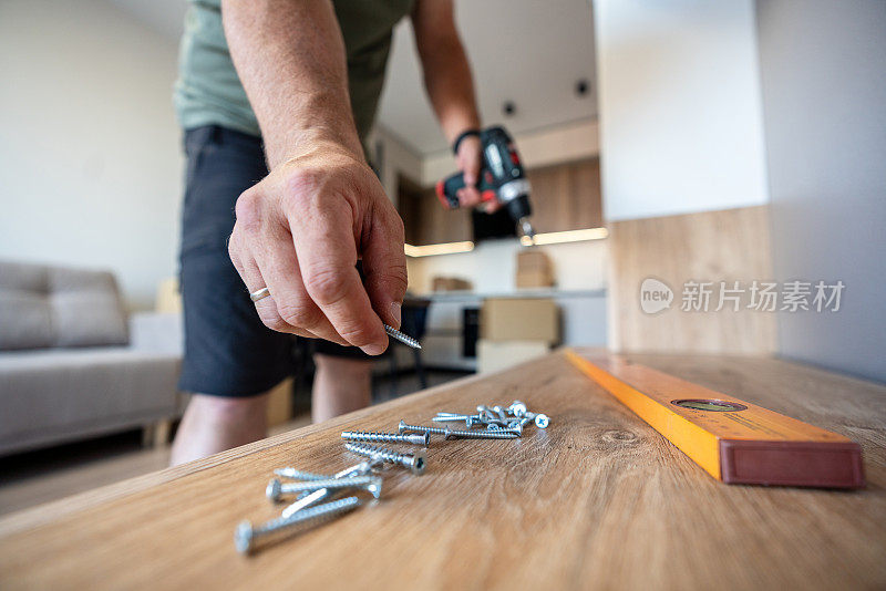 一个人拿着电动螺丝刀从架子上取下一个螺丝，在家里的客厅里组装家具