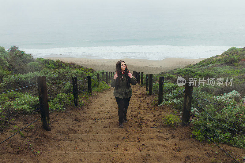 一名女子在考虑下雨天的事，她走在加州旧金山的海滩上