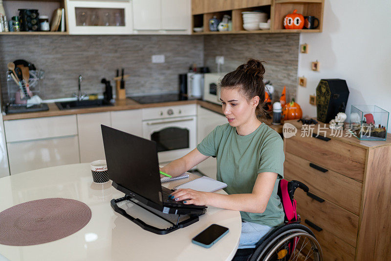 坐在轮椅上的年轻女子在家用笔记本电脑工作。