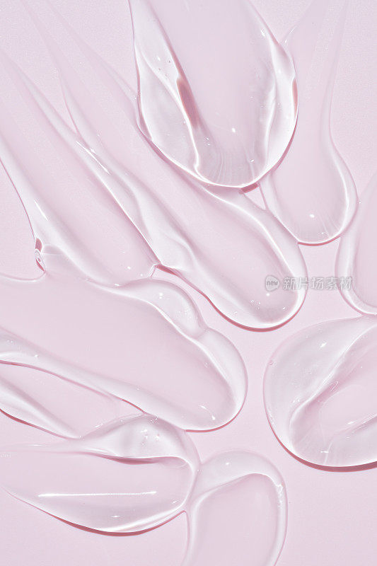 液体凝胶涂片分离在粉红色背景。美容化妆品污物，如纯透明芦荟乳液，面部啫喱精华液，洗面奶，沐浴露或洗发水俯视图。