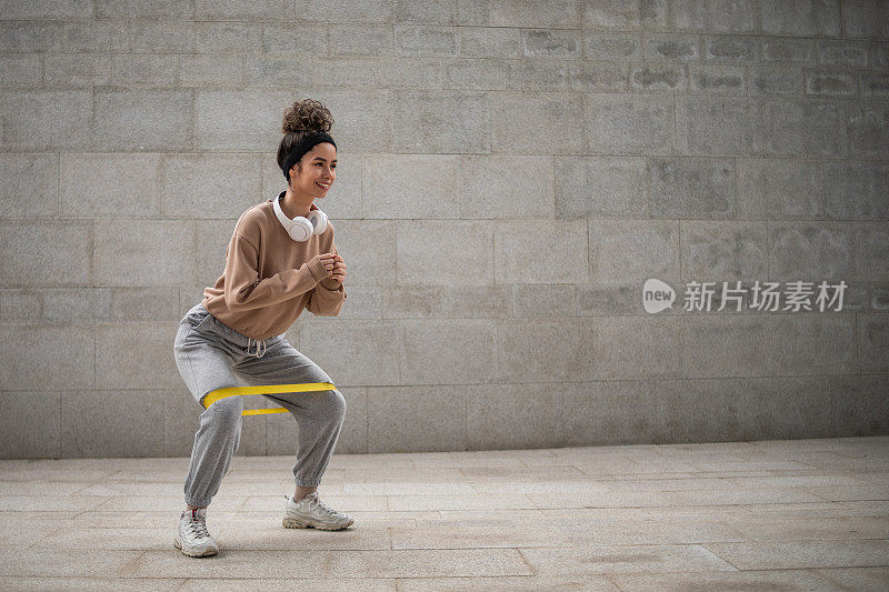 一位年轻的女运动员在户外用橡皮筋做深蹲训练