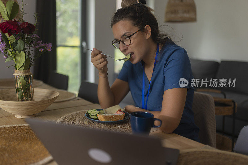一名女医务工作者坐在家里的餐桌旁，休息一下，吃着早餐
