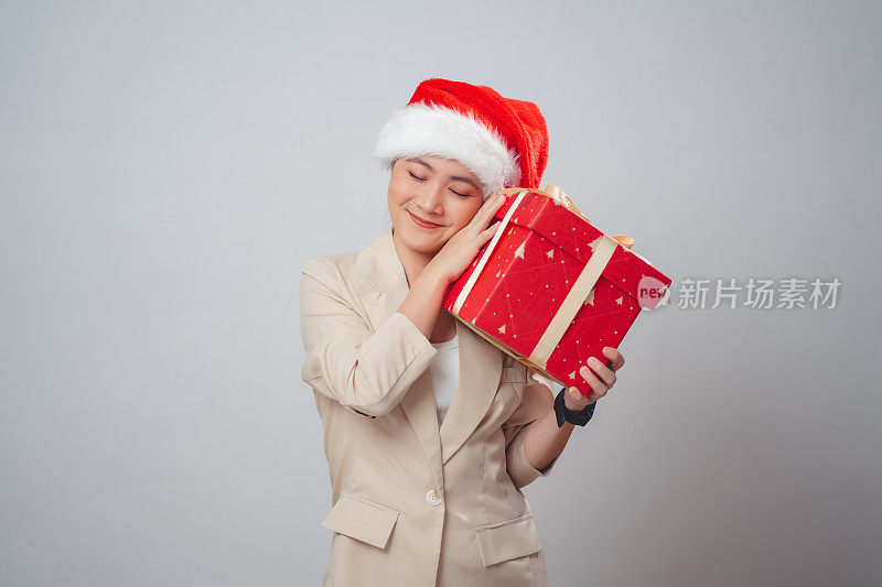 亚洲女人戴着圣诞老人的帽子，拿着礼盒开心地微笑，孤立在白色的背景上。