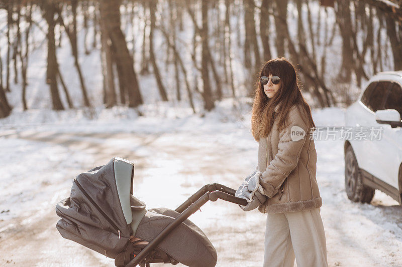 在一个阳光明媚的冬日，一位年轻的母亲推着婴儿车在公园里散步。