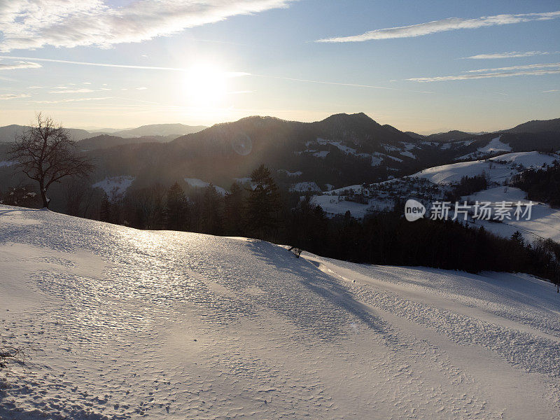 日落时的冬日风景，白雪覆盖的山丘和晴朗的天空。