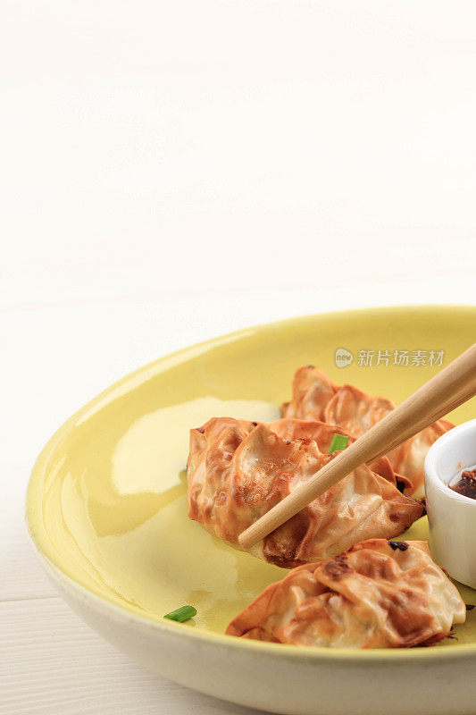 Gyoza亚洲锅贴，用黄色的陶瓷盘子和白色的木制背景，用筷子和葱。没有油的空气炸锅烹饪。