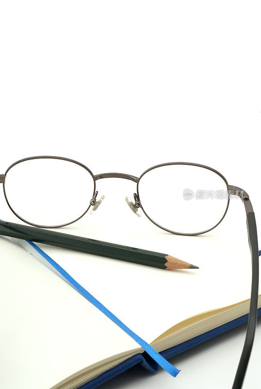 桌上放着笔记本，眼镜和铅笔