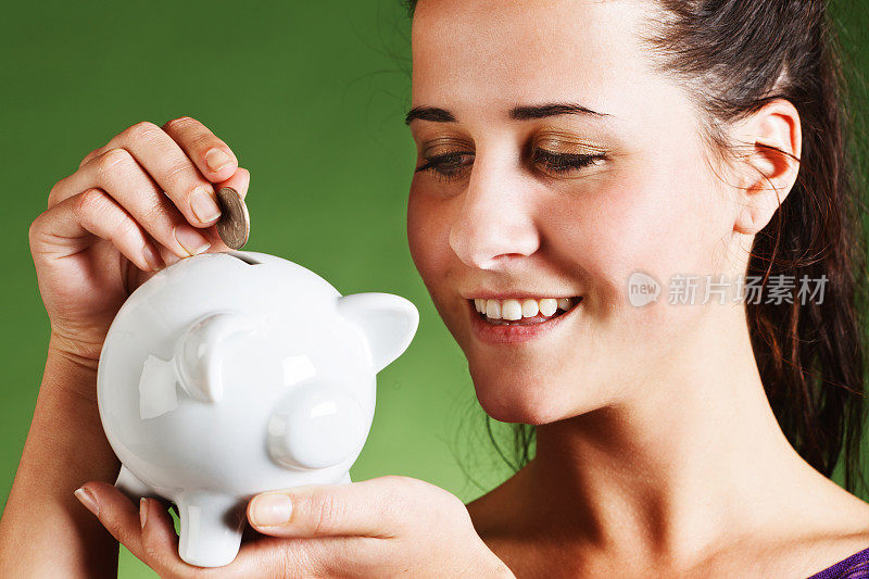 微笑的年轻褐发女子把硬币放入存钱罐