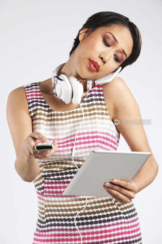女人拿着手机，数字平板电脑，遥控器和耳机