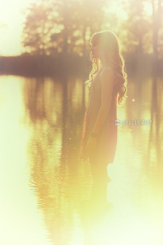 沉思的年轻女子涉水在湖在日落