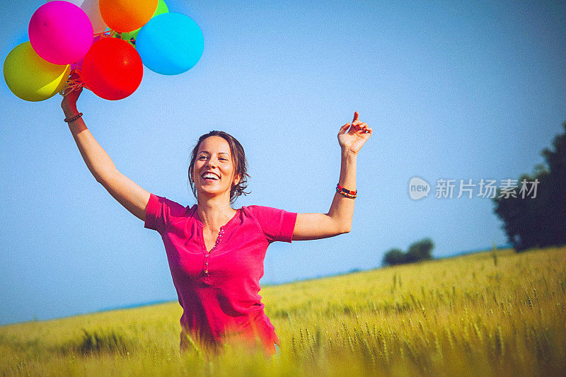 兴高采烈的女人拿着彩色的气球，跑过麦田