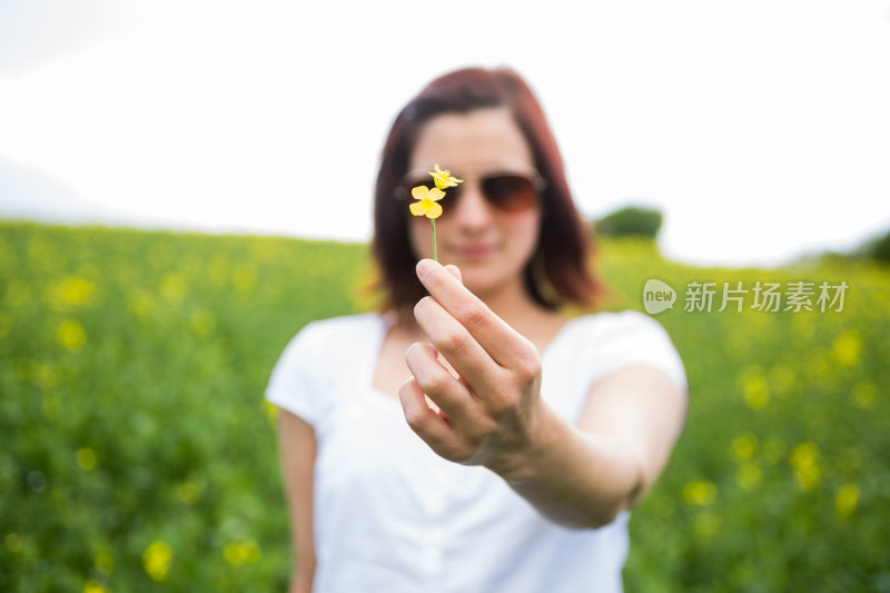 一个平静的年轻女子，手里拿着一朵小小的黄花