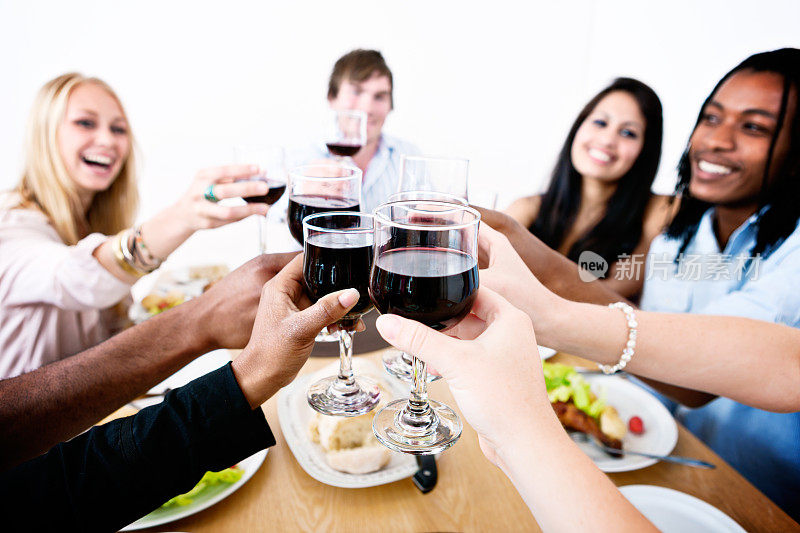 微笑的年轻人围坐在餐桌旁用红酒祝酒