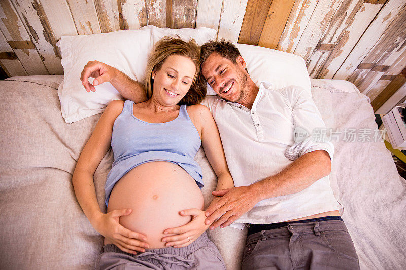 一对夫妇躺在床上抚摸着妇女怀孕的肚子