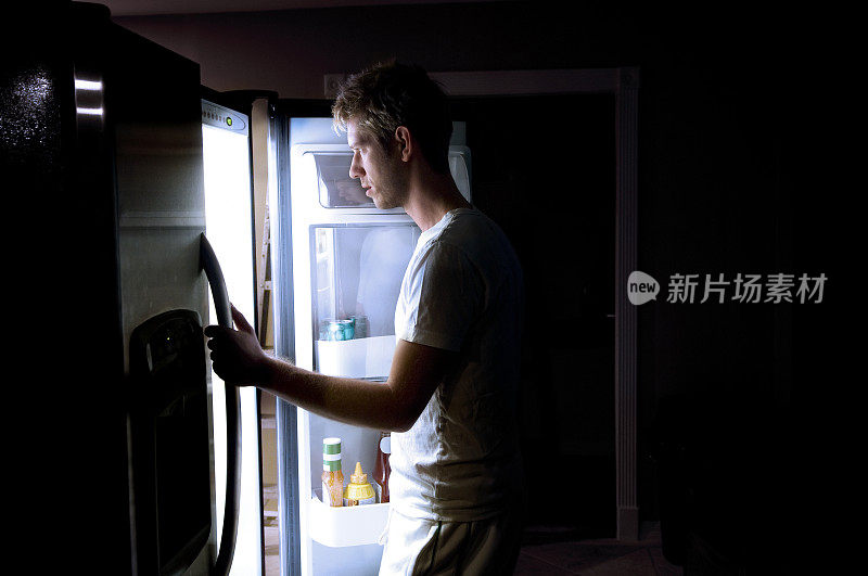 一个男人在看一个周围没有灯的冰箱里