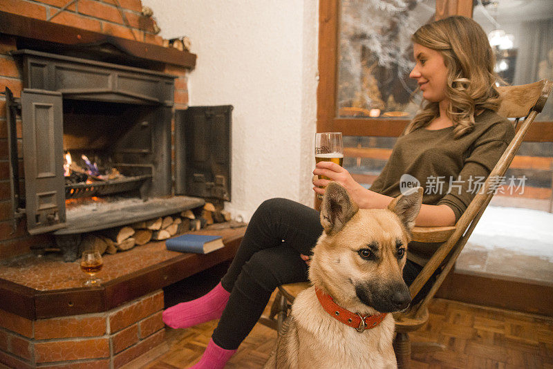 拿着一杯啤酒和一条狗的女人站在壁炉旁边