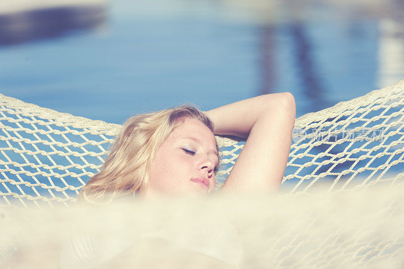 一个美丽的女人躺在游泳池旁的吊床上。