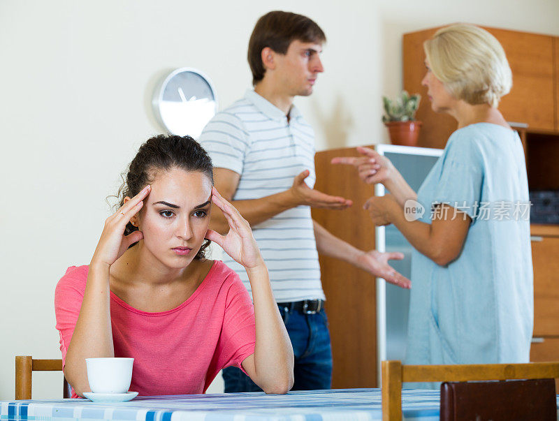 悲伤的年轻女人看着丈夫和母亲吵架