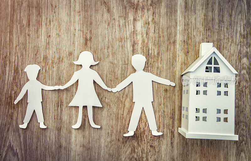 家庭和家庭的概念。纸上的爸爸、妈妈和儿子手牵着手靠近木制的微型房子。