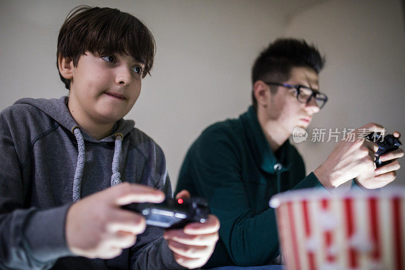 两个迷人的少年坐在家里的沙发上玩游戏机，面带微笑