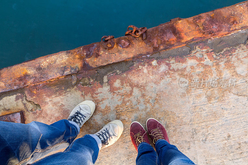 一个男人和一个穿着牛仔裤和运动鞋的女孩站在一个生锈的码头上。