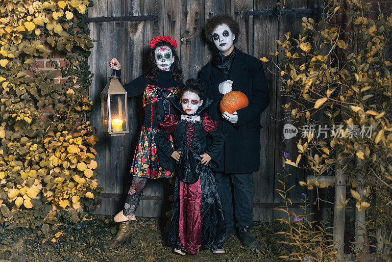 三个孩子穿着诡异的万圣节服装站在老房子前
