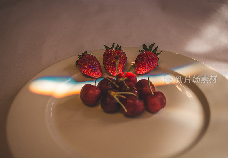 白色的盘子上放着樱桃和草莓，彩色的光线