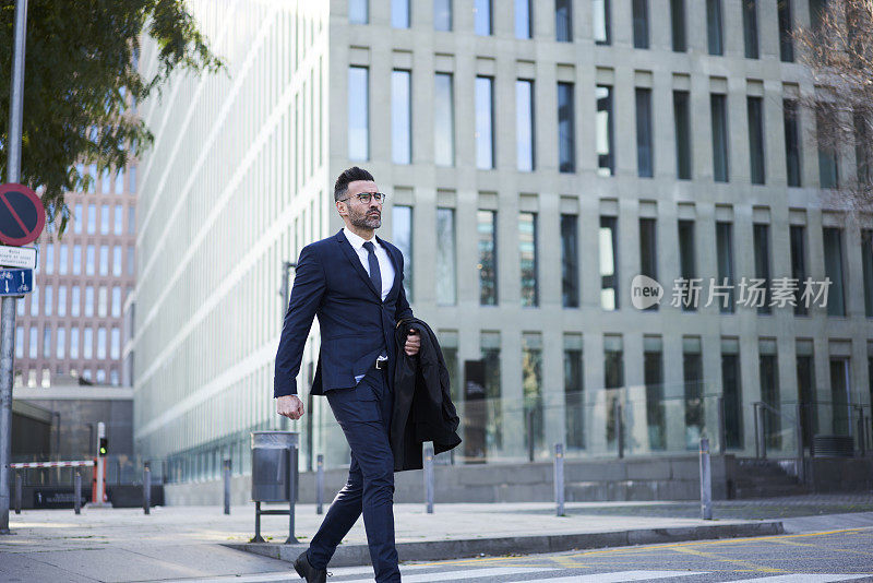 成熟的男企业家穿着优雅的西装在大都市商业区的十字路口散步，帅气的职业经济学家自信地赶着开会