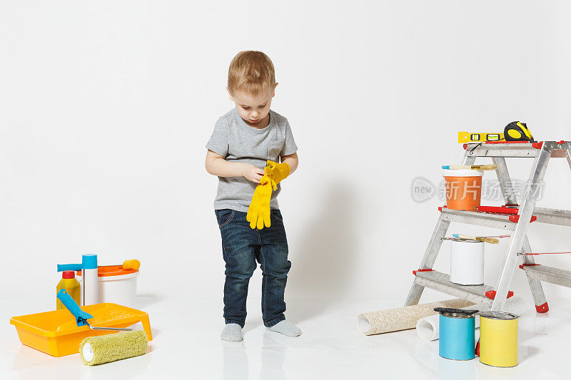 可爱的小男孩戴着黄色手套，用仪器装修公寓房间，隔离在白色的背景上。墙纸，胶水配件，绘画工具。修复。为人父母,童年的概念。