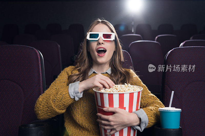年轻兴奋的女人戴着3d眼镜，拿着一大篮爆米花在电影院看电影