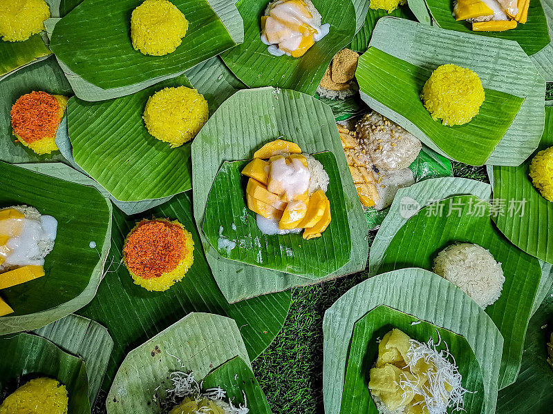 泰国芒果糯米饭和其他著名的新鲜的泰国甜点放在香蕉叶上，在一个典型的泰国市场出售。