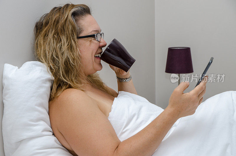 女人在她的酒店床上喝咖啡，同时看她的手机白天