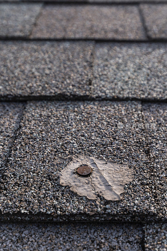 一个住宅沥青瓦屋顶上的一个坏补丁的特写，露出钉子头