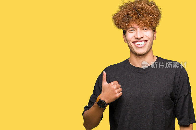 年轻英俊的男子与非洲发式穿着黑色t恤做快乐的拇指手势与手。赞许的表情看着镜头，表示成功。