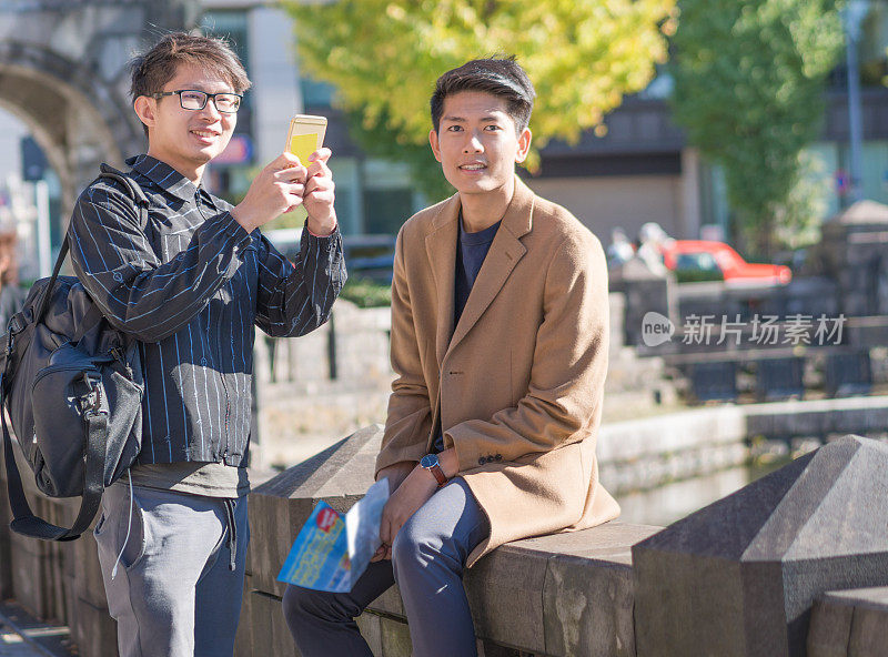 年轻的亚洲男子和日本朋友寻找旅游地点使用手机和花时间在亚洲旅行